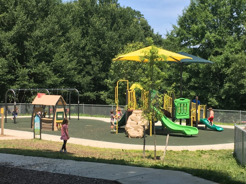 Children play on a brightly colored playground structure that includes a yellow canopy and two green slides.