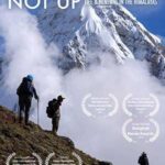 A film poster shows three people hiking on a steep brown slope. Behind them are clouds, a snowy mountain, and blue sky. The words LOOK DOWN NOT UP are in white at the top of the screen. In the bottom and middle of the screen, around the people, are the listings of film awards surrounded by laurel leaves.