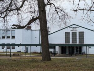 A white building. The words DORA KENNEDY FRENCH IMMERSION appear at right, just below a peaked roof. At left, a section with a flat roof. In front, a tree. 