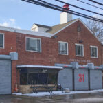 A red brick building with five large grey garage doors. "31" in red numbers on the central garage door.