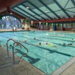 Swimmers lap-swimming in the swimming pool below a peaked blue roof.