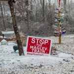 A red and white yard sign reading STOP THE MAGLEV TRAIN, StopThisTrain.org, in a snowy yard.