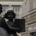 A black statue of two people, next to a beige stone building with US AGENCY FOR INTERNATIONAL DEVELOPMENT on the side.